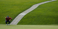 Ein Golfspieler hockt auf einem Golfplatz, im Hintergrund ein Weg