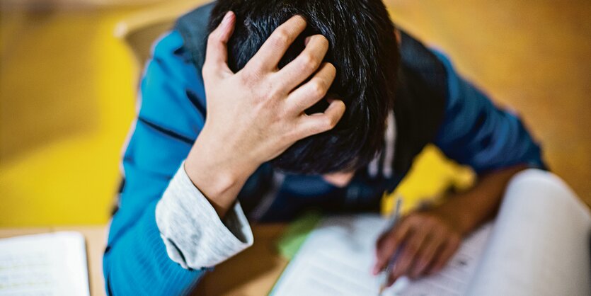 Ein Schüler schreibt in ein Heft und rauft sich dabei die Haare