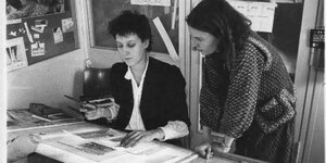 Françoise Cactus und Rita Hermanns kleben an einem Schreibtisch das Layout der taz