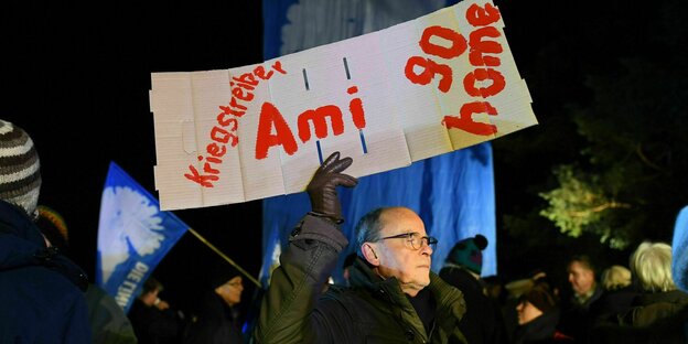ein Demonstrant hält ein Schild hoch: Ami go home