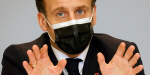 Macron zuckt die Schultern und streckt abwehrend die Hände aus.