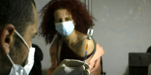 Frau mit Mundschutz erhält gleich eine Sprizte - Es ist der Corona-Impfstoff