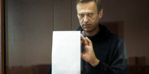 Nawalny im Angeklagten-Glaskasten. Er drückt ein weißes Blatt Papier gegen die Scheibe.