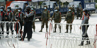 Bewaffnete Polizisten und Soldaten hinter einer Stacheldrahtsperre