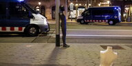 Eine Schaufensterpuppe steht an einen Laternenpfahl gelehnt vor zwei Polizeiwagen