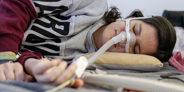 Annika Braun liegt auf dem Bett, trägt ihre Atemmaske und schläft Annika Braun liegt auf dem Bett, trägt ihre Atemmaske und schläft