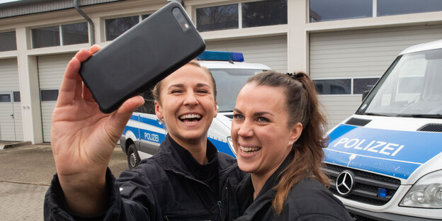 Zwei Polizistinnen posieren lachend mit dem Smartphone für ein Selfie.