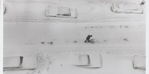 Verschneite Straße mit geparkten Autos links und rechts und in der Straße läuft ein Mann, der im Schnee Fußstapfen hinterlässt