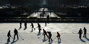 Mehrere Eisläufer am Engelbecken in Berlin. Ein paar spielen Eishockey.