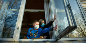 Zwei Kinder mit Mundschutz öffnen ein Fenster