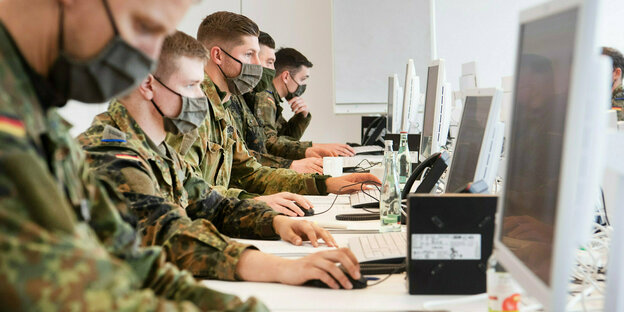 Bundeswehrsoldaten sitzen in einer Reihen mit Masken an Computern