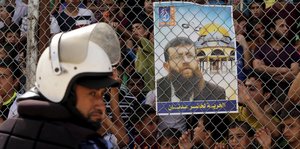 Ein Polizist läuft an einem Plakat mit dem Bild von Khader Adnan vorbei