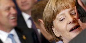 Bundeskanzlerin Angela Merkel flüstert einem Mann etwas ins Ohr.