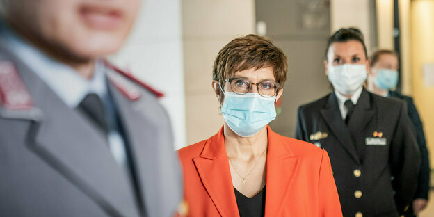 Annegret Kramp-Karrenbauer, die Bundesministerin für Verteidigung, zwischen zei Männern in Uniform. sie trägt einen Blazer, Mund-Nasenschutz und eine Brille. Sie ist eine ältere Frau mit kurzen Haaren.