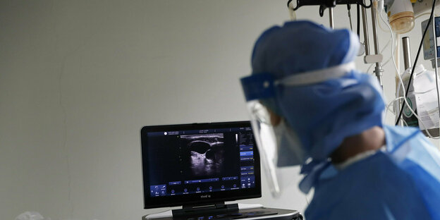 Eine Person in Svchutzkleidung schaut auf einen Monitor auf dem ein Ultraschallbild zu sehen ist