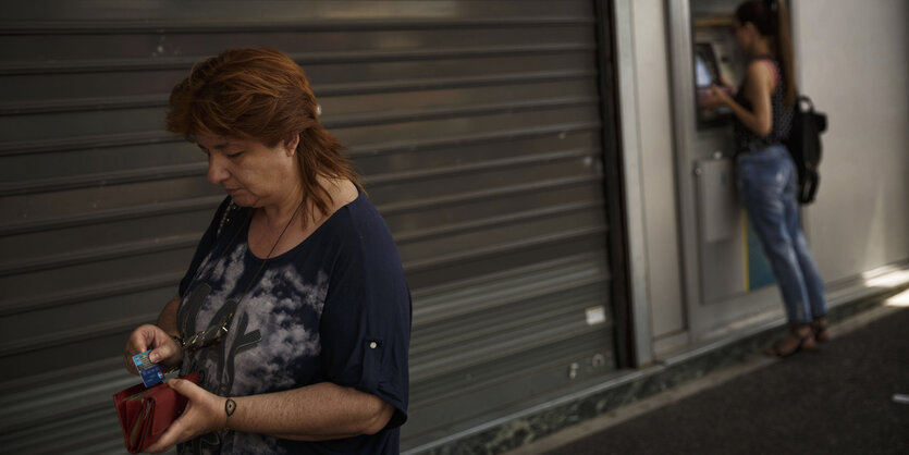 Eine Frau steckt Geld ein, eine ander Frau steht am Bankautomaten