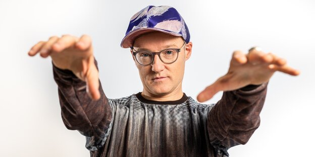 Der Musiker PeterLicht steht mit ausgestreckten Händen da und hat ein Käppi auf dem Kopf Der Musiker PeterLicht steht mit ausgestreckten Händen da und hat ein Käppi auf dem Kopf