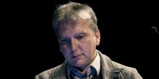 Mark Fisher gestikuliert lächelnd im grauen Jacket vor Mikro