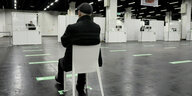 Eine Person sitz in einer leeren Halle auf einem Stuhl.
