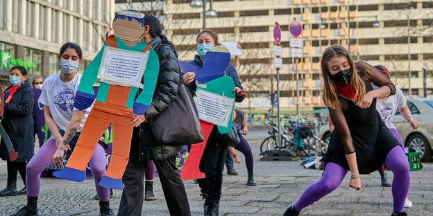 Eine Gruppe von tanzenden Aktivist:innen mit Schildern vor der Senatsverwaltung am Alexanderplatz