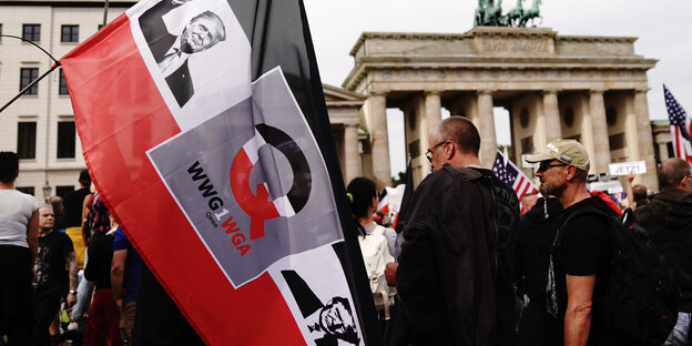 Auf einer schwarzweißroten Fahne, die ein Teilnehmer vor dem Brandenburger Tor hält, sind ein Bild von Trump und der Buchstabe "Q" aufgedruckt.
