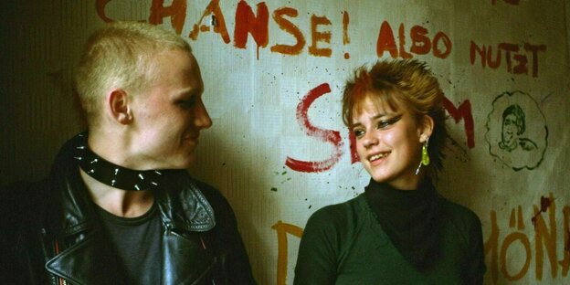 Punker und Punkerin stehen vor einer bemalten Wand und lächeln sich an