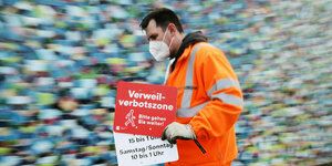 Ein Mitarbeiter der Düsseldorfer Verkehrsbetriebe geht mit einem Verbotsschild "Verweilverbotszone - Bitte gehen Sie weiter"
