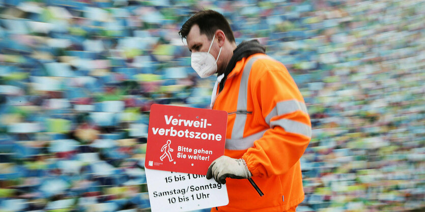 Ein Mitarbeiter der Düsseldorfer Verkehrsbetriebe geht mit einem Verbotsschild "Verweilverbotszone - Bitte gehen Sie weiter"