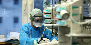 Krankenhauspersonal in voller Schutzmontur versorgt einen Covid-19 Patienten