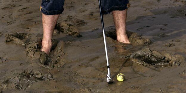 Golfspieler mit den Füßen im matschigen Nordseeschlick versucht Ball zu treffen