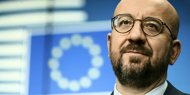 Charles Michel steht vor einem Hintergrund mit Europaflagge und blickt leicht nach oben