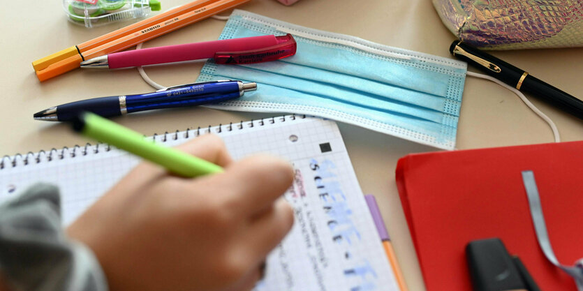 Kinderschreibtisch mit Hand, die einen Stift hält und etwas in ein Heft schreibt