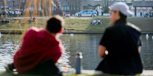 Zwei Menschen sitzen am Ufer des Landwehrkanals, im Hintergrund ein Polizeiauto
