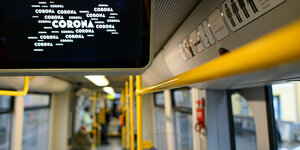 In einer Straßenbahn sind nur wenige Fahrgäste. Auf einer Anzeigetafel steht das Wort Corona.