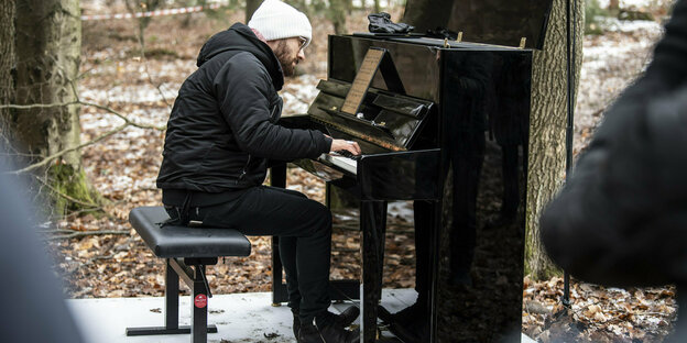 Der Pianist Igor Levit sitzt im Wald an einem schwarzen Klavier