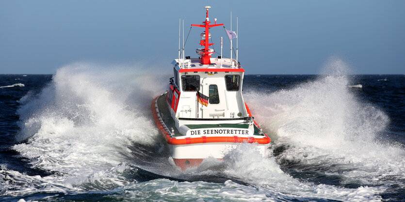 Ein Boot der Seenotretter ist zu sehen, von hinten, auf dem Wasser, links und rechts spritzt das Wasser