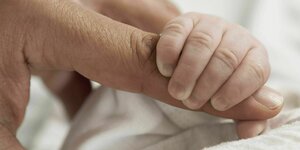 Die Hand eines Neugeborenes umgreift einen Finger