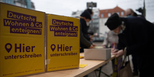 Ein Stand der Initiative Deutsche Wohnen und Co enteignen. Zu sehen sind zwei Plakate, auf denen zum Unterschreiben aufgefordert wird. Im Hintergrund unterschreibt eine Frau.