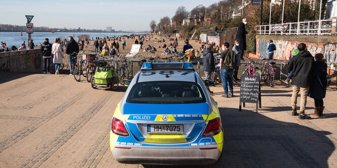 ein Polizeiauto steht am Elbstrand, daneben viele Passant:innen