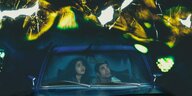 Es ist dunkel, ein Paar sitzt in einem Auto, von oben regnet es gheimnisvolles Licht