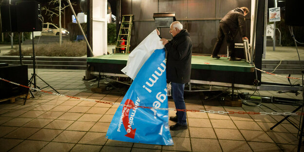 Ein AfD-Helfer faltet ein blaues Wahlplaket zusammen