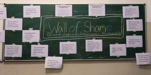 "Wall of Shame" steht in Kreide groß auf der Tafel. Daneben kleben Zettel, auf denen Schüler:innen ihre Erfahrungen mit Sexismus beschreiben.