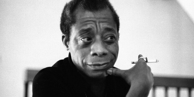 Schwarzweißaufnahme des Schriftstellers James Baldwin, der einen ring am Zeigefinger trägt und eine Zigarette hält.