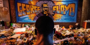 Ein Mann genenkt George Floyd vor einem großen Graffitti in Minneapolis welches George Floyd zeigt
