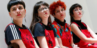 Vier junge Frauen in dunklen T-Shirts und roten Latzhosen