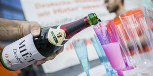 Ein Mitglied von Attac gießt vor dem Eingang zur Hauptversammlung des Immobilienkonzerns Deutsche Wohnen Sekt aus einer Flasche ein, deren Markenname in "Miet Deckel" umbenannt wurde.