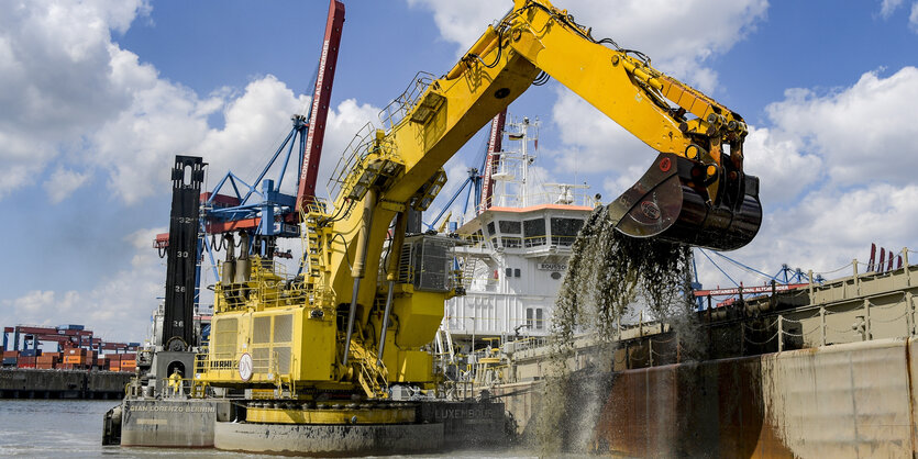 Ein Bagger hebt mit seiner Schaufel Hafenschlick aus einem Becken