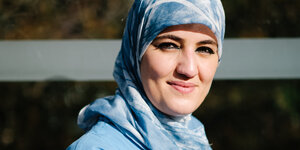 Farah Demir trägt helblaue Arbeitskleidung, ein Kopftuch und lächelt in die Kamera