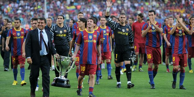 Präsident Laporta trägt mit Messi Pokal über den Rasen, Team im Hintergrund