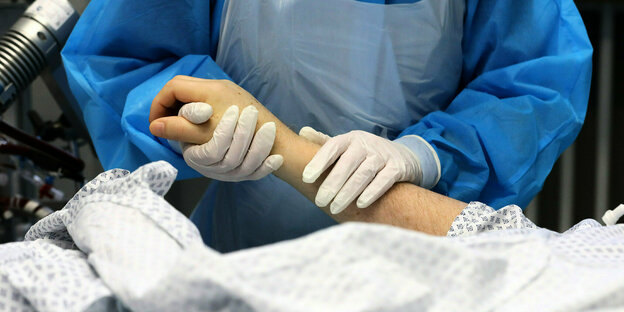 Eine Krankenhausmitarbeiterin hält die Hand eines Covid-19 Patienten